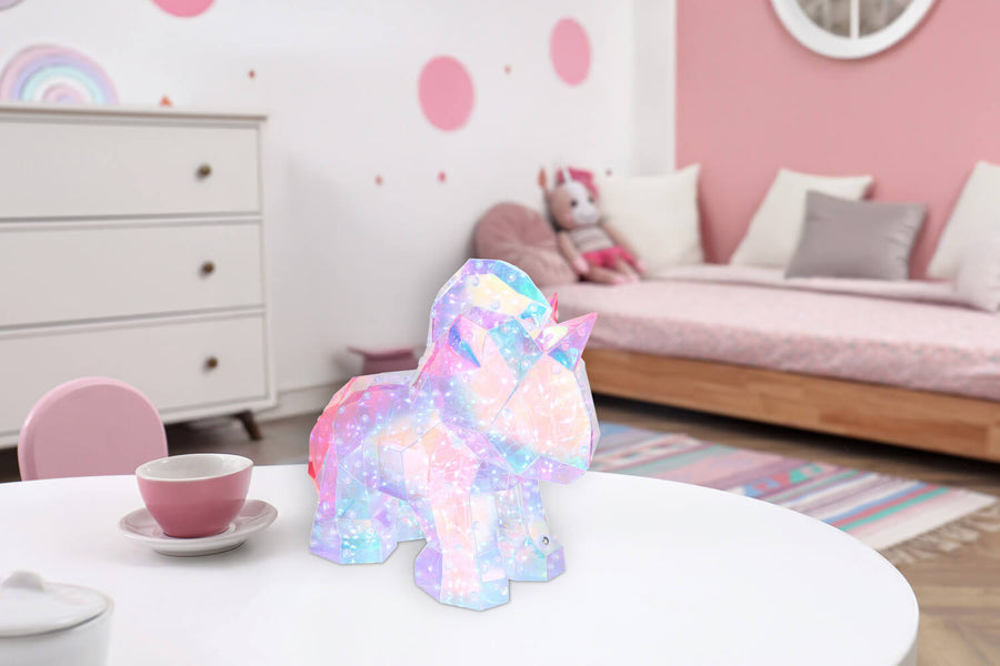 Lampe licorne posée sur table blanche dans une chambre enfantine rose.