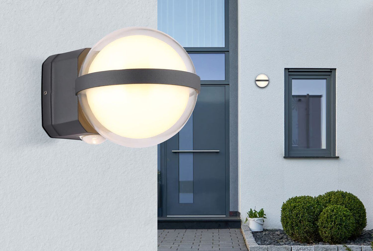 Luminaire anthracite allumé près d'une porte d'entrée moderne sur mur crème