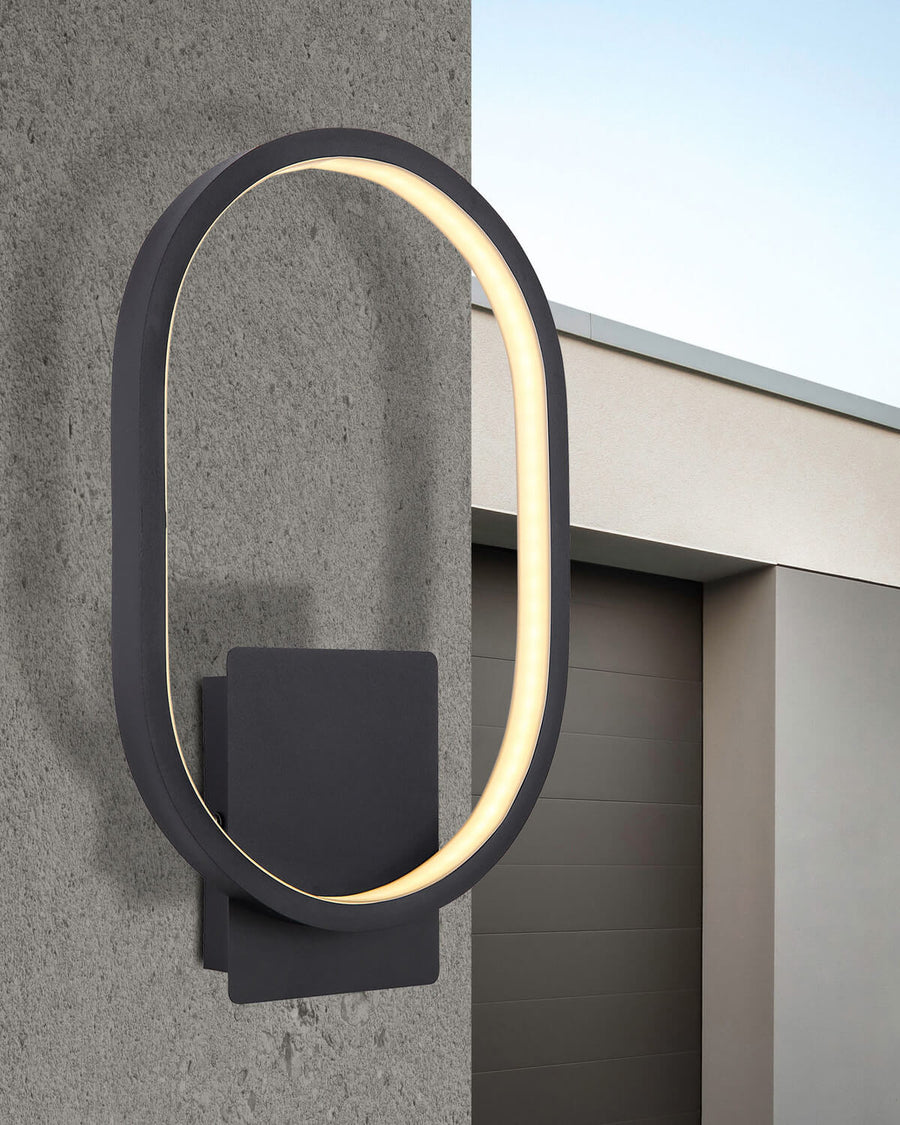 Luminaire mural ovale noir installé sur un mur extérieur gris, éclairant une entrée de garage