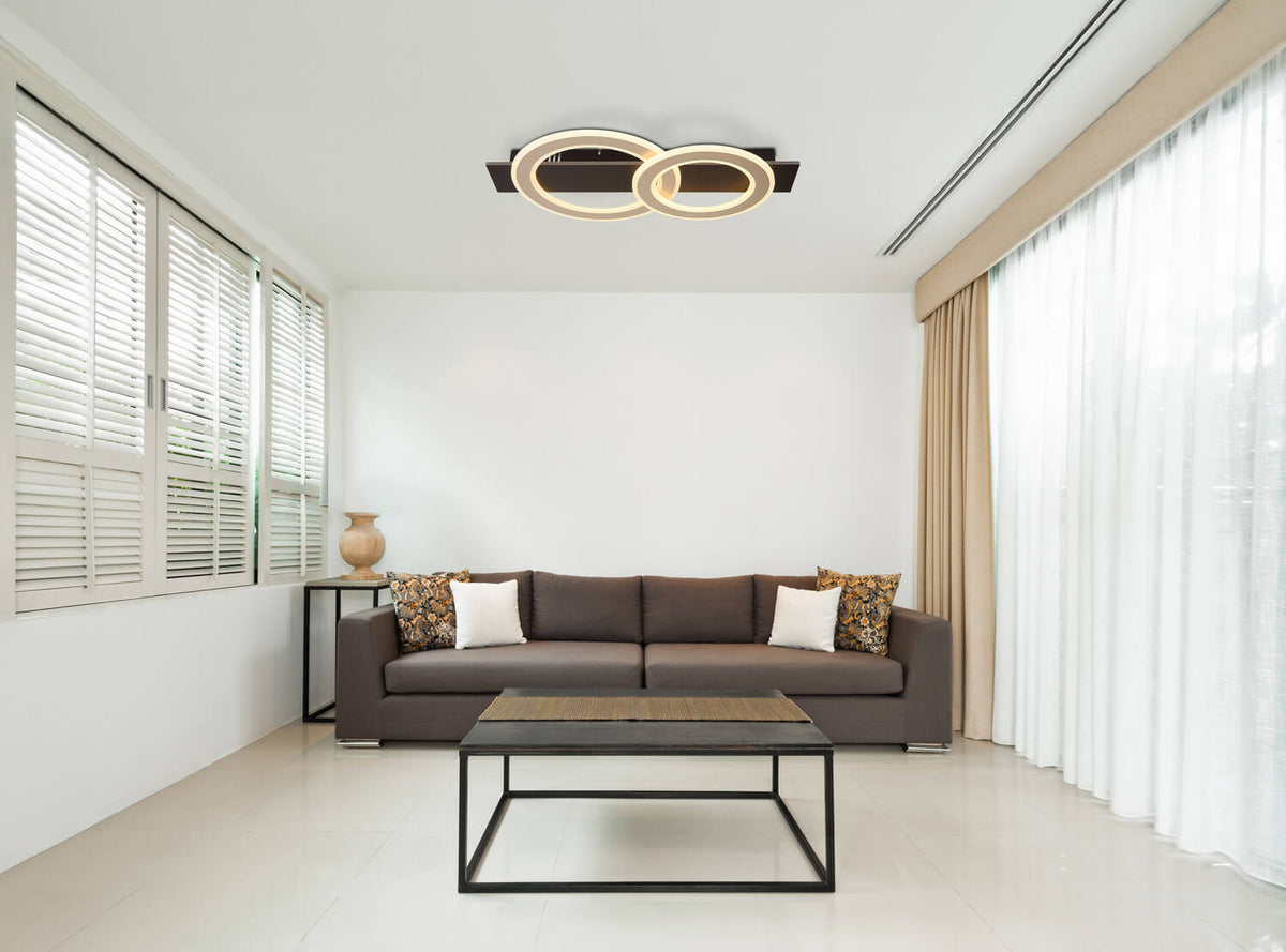 Mise en ambiance dans un salon moderne, plafonnier allumé au-dessus d'un canapé brun.