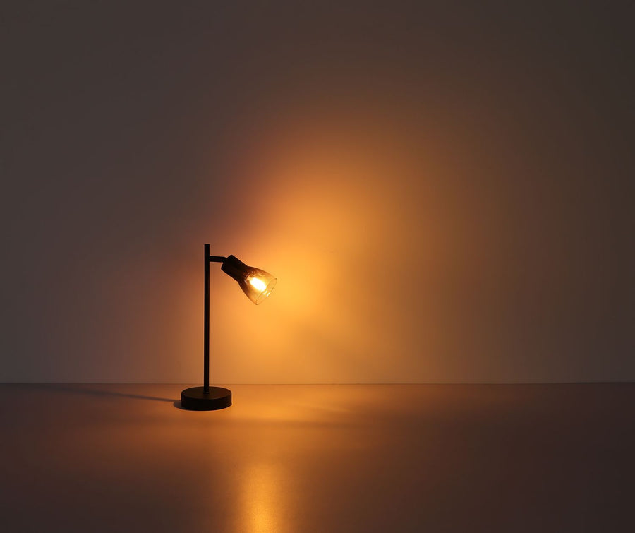 Lampe de table noire allumée dans l'obscurité, halo de lumière chaude au mur