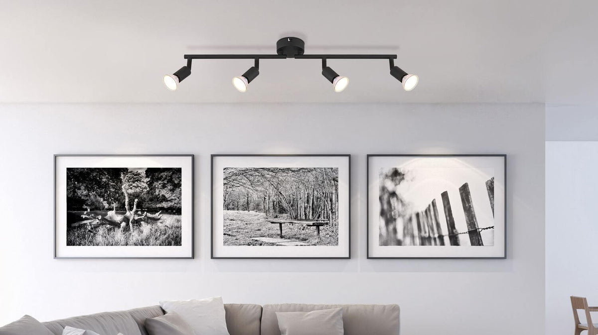 Luminaire noir mat fixé au plafond, éclairant trois cadres photo dans un intérieur clair.