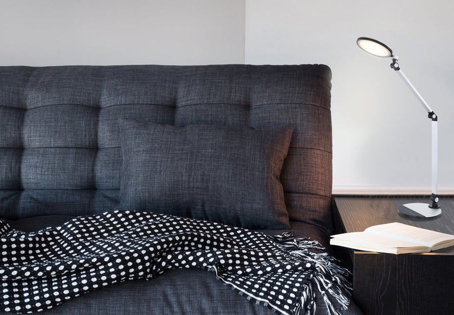 Lampe posée sur table de chevet, près d'un livre ouvert, dans une chambre.