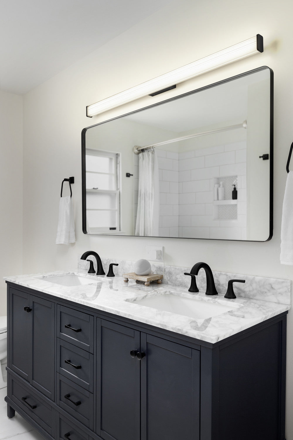 Mise en ambiance salle de bain : applique allumée au-dessus du miroir et du meuble vasque