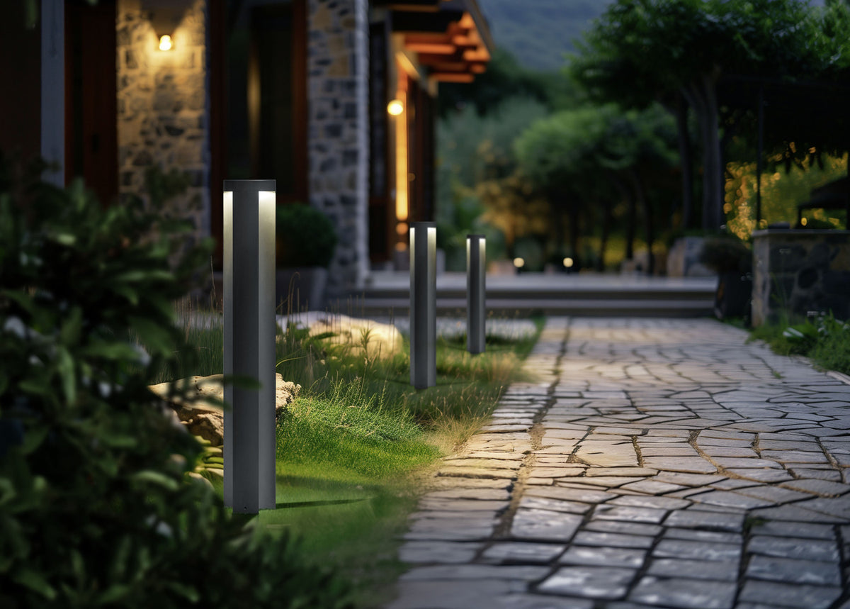 Mise en ambiance nocturne, plusieurs bornes anthracite alignées le long d'une allée pavée