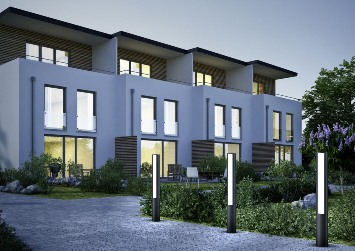 Trois bornes anthracite éclairées le long d'une allée devant une maison moderne