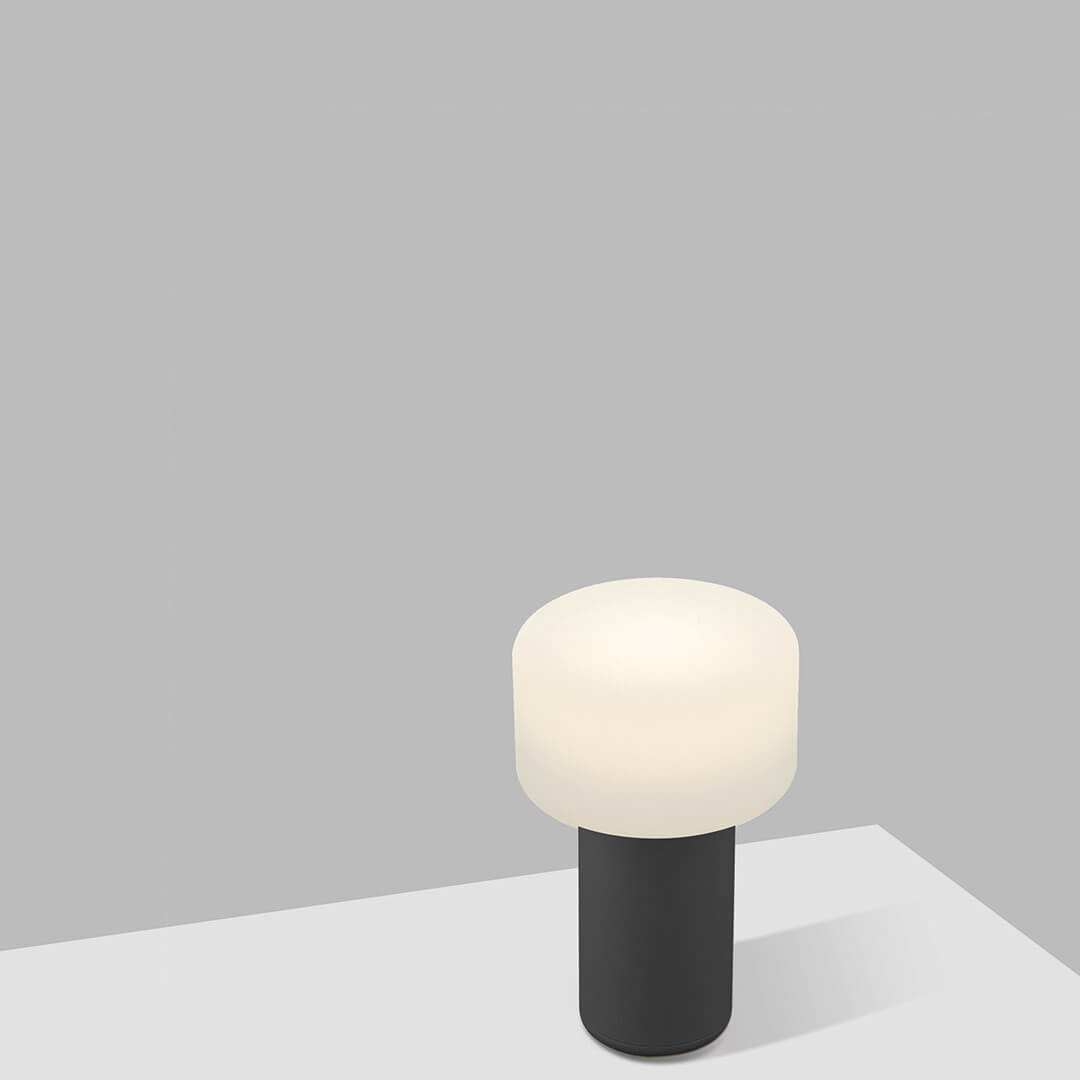 Mise en ambiance sur une table, lampe allumée devant un mur gris clair