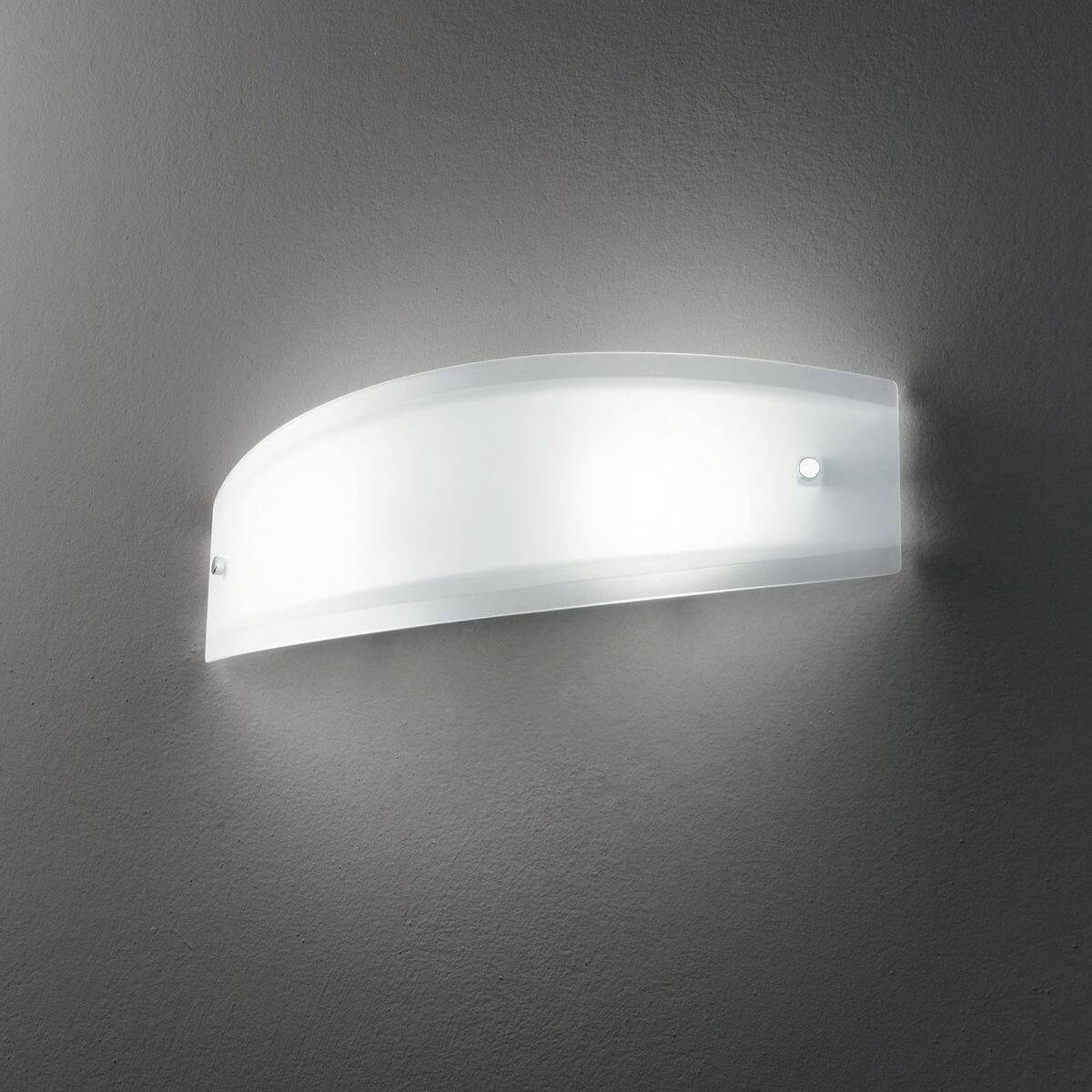 Mise en ambiance : applique allumée sur mur gris foncé, halo lumineux diffus