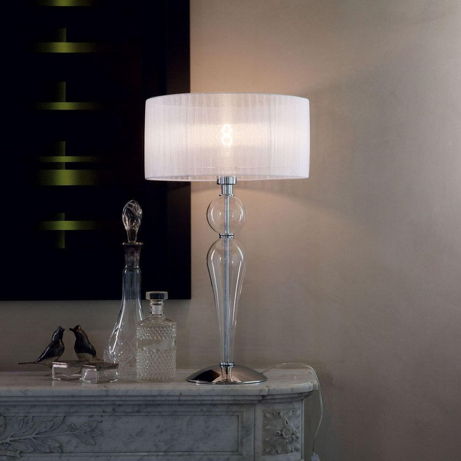 Lampe allumée posée sur une commode en marbre, entourée de flacons et d'oiseaux décoratifs