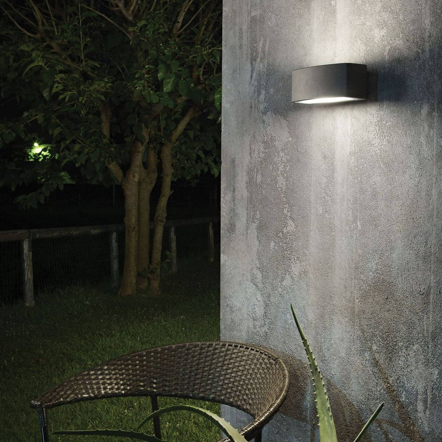 Mise en situation nocturne sur mur béton, arbre et fauteuil en résine tressée