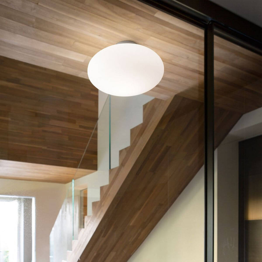 Plafonnier blanc allumé, installé sur plafond en bois au-dessus d'un escalier vitré.