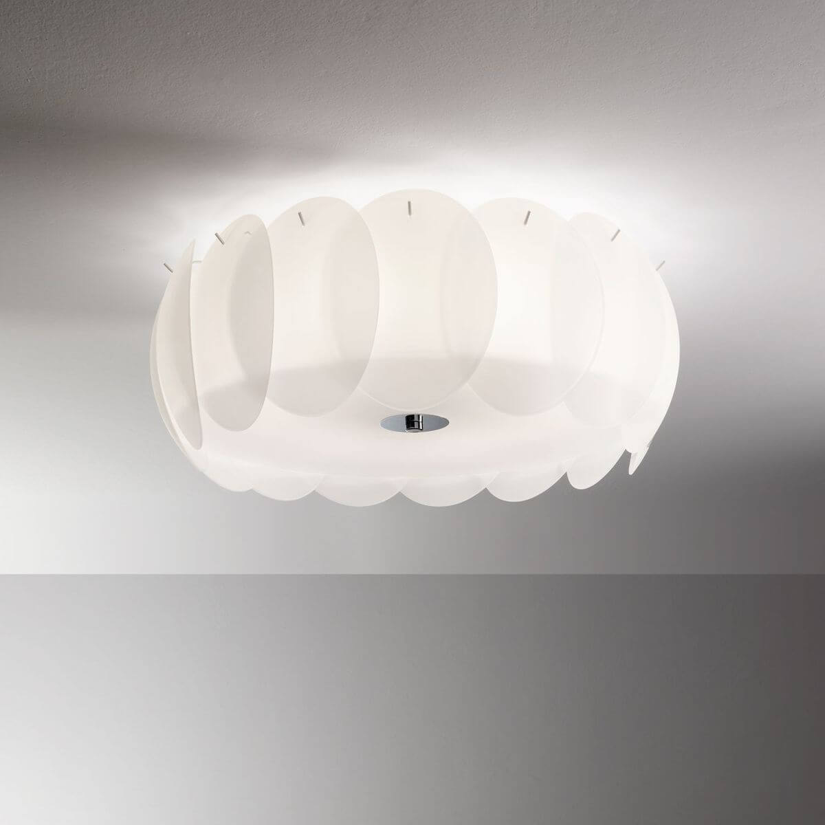 Plafonnier blanc allumé fixé au plafond, diffuseurs en verre superposés en ambiance.