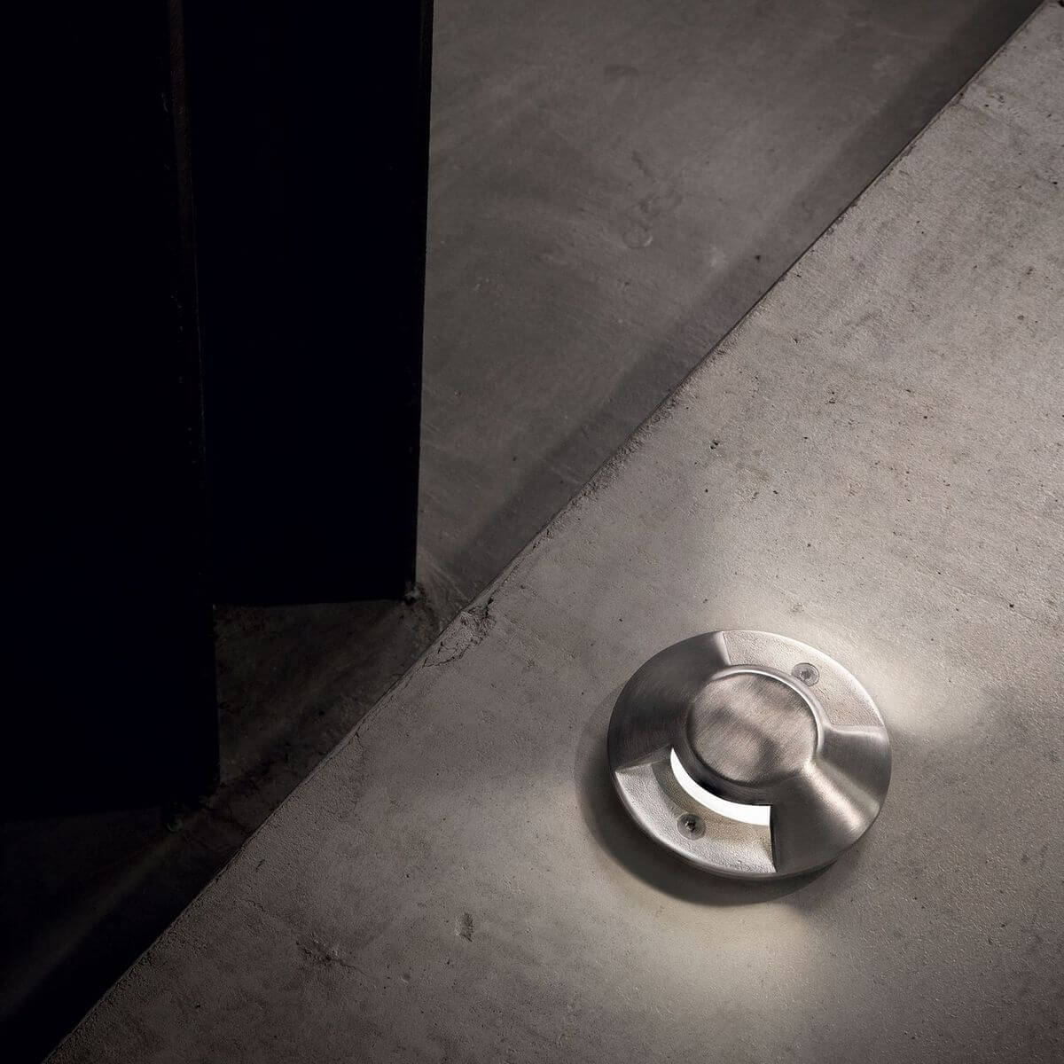 Spot encastré au sol éclairé dans une pièce en béton ciré