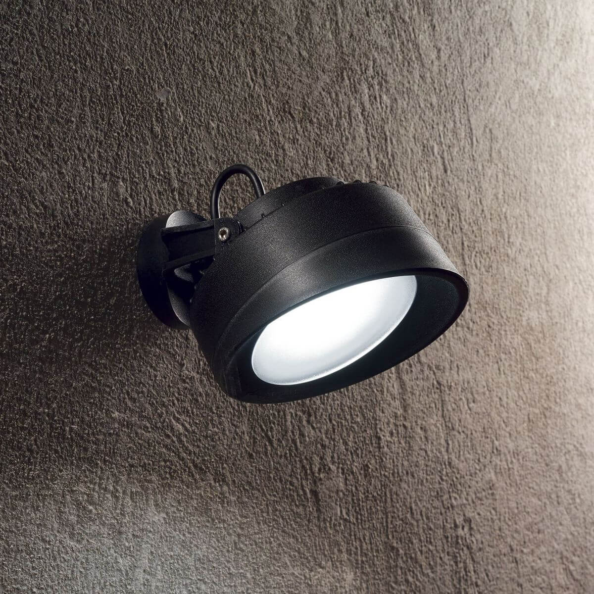 Luminaire mural noir allumé, fixé sur un mur texturé en extérieur