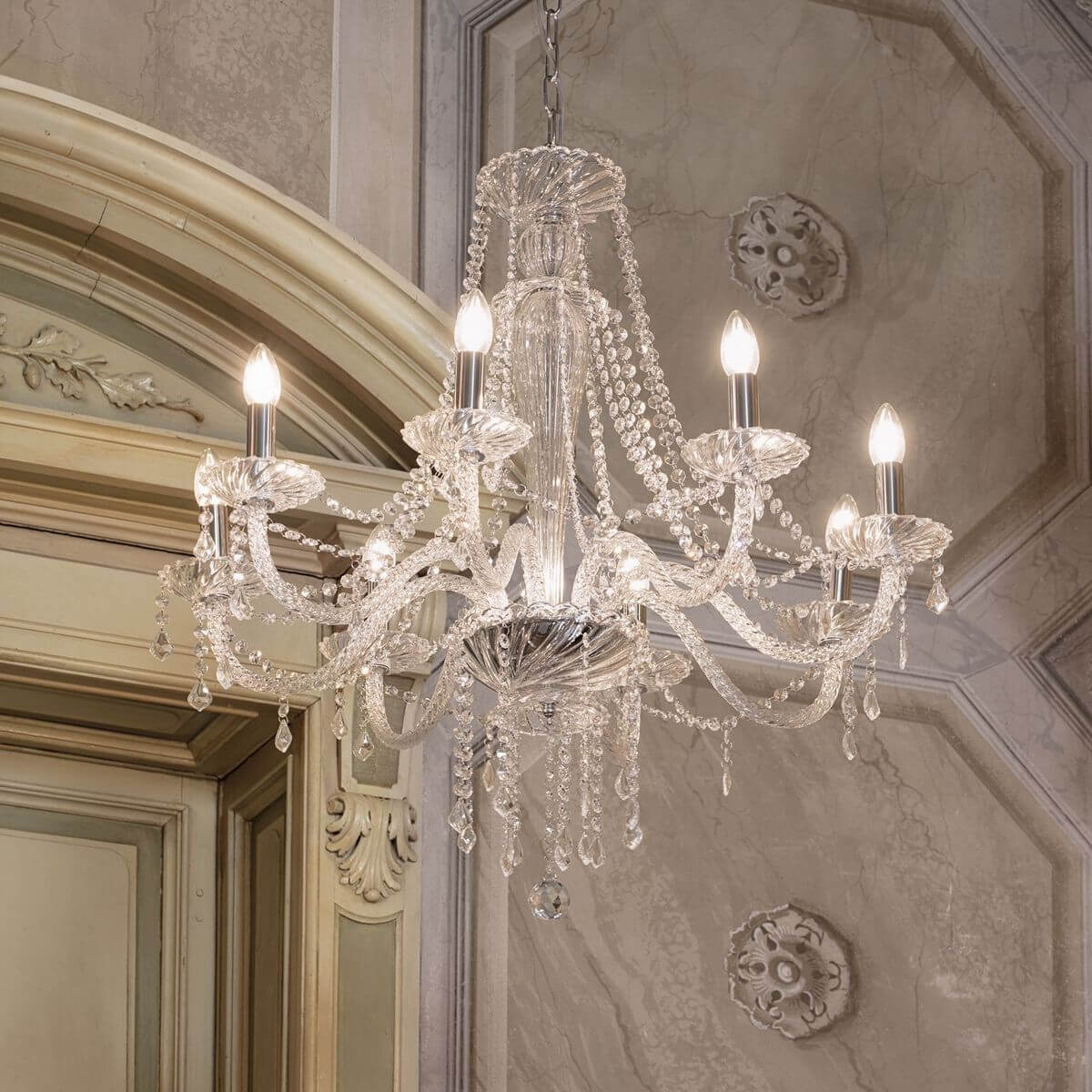 Chandelier en cristal allumé, suspendu dans un intérieur classique avec moulures et décorations murales.