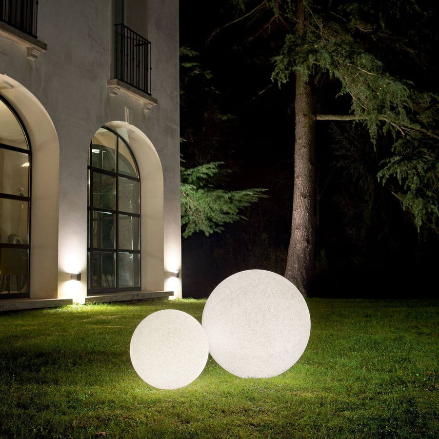 Deux sphères lumineuses blanches posées sur une pelouse devant une maison la nuit