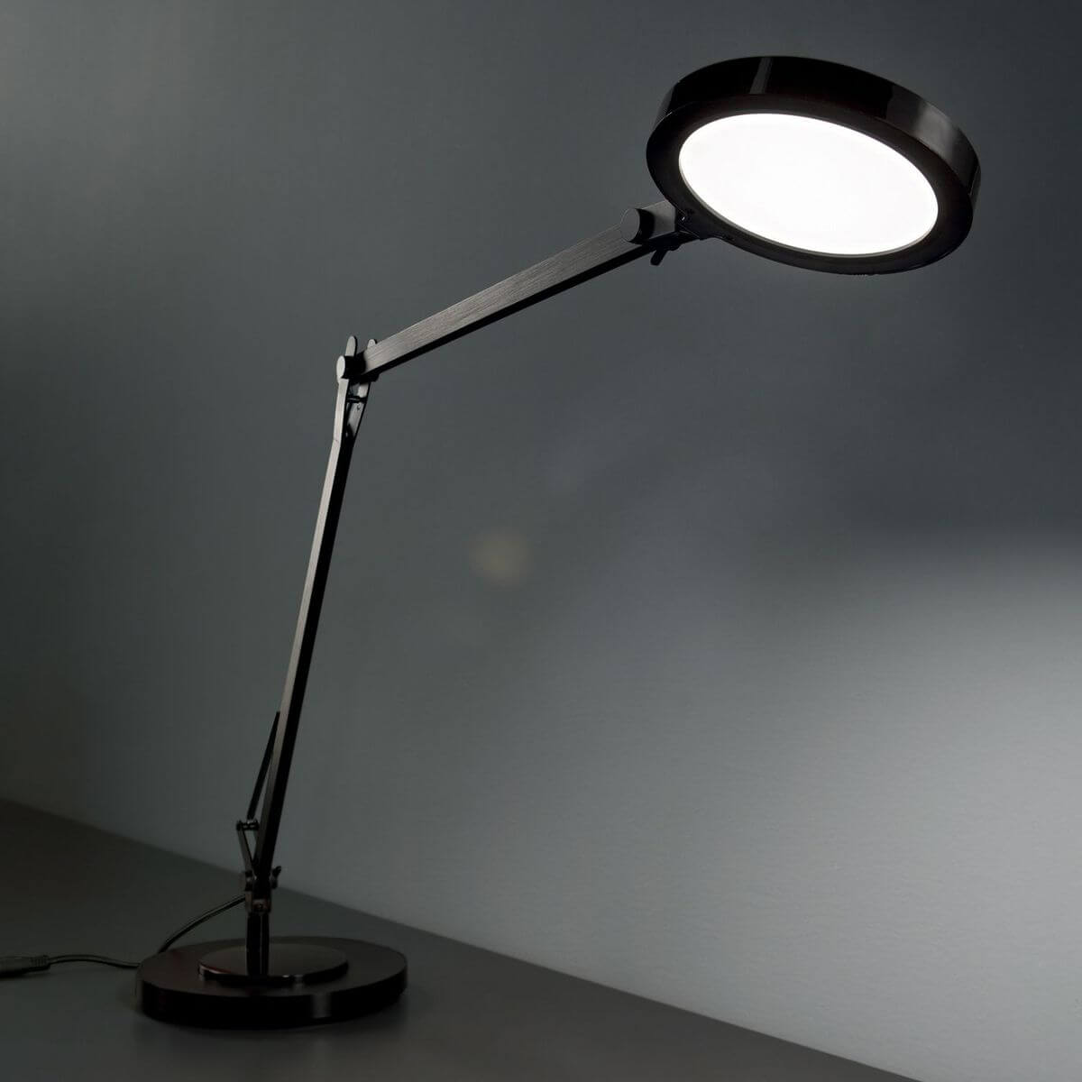 Lampe noire allumée posée sur un bureau sombre, diffuseur rond lumineux en ambiance