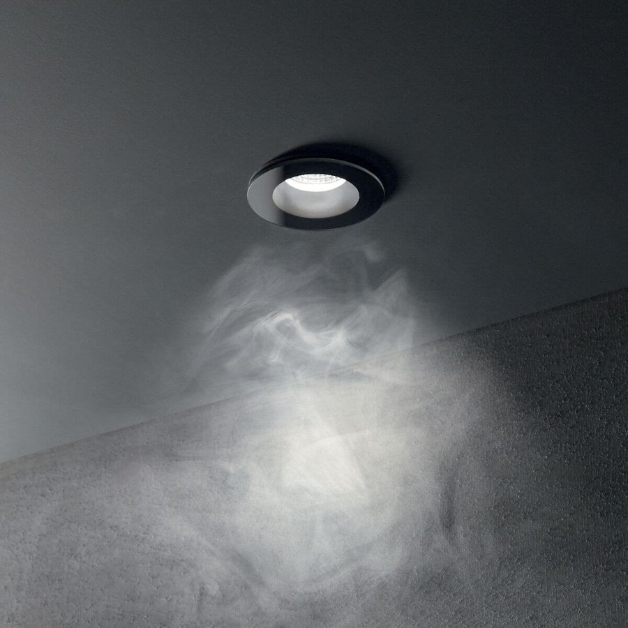 Spot noir encastré au plafond, éclairant la pièce avec un faisceau lumineux traversant une fumée.