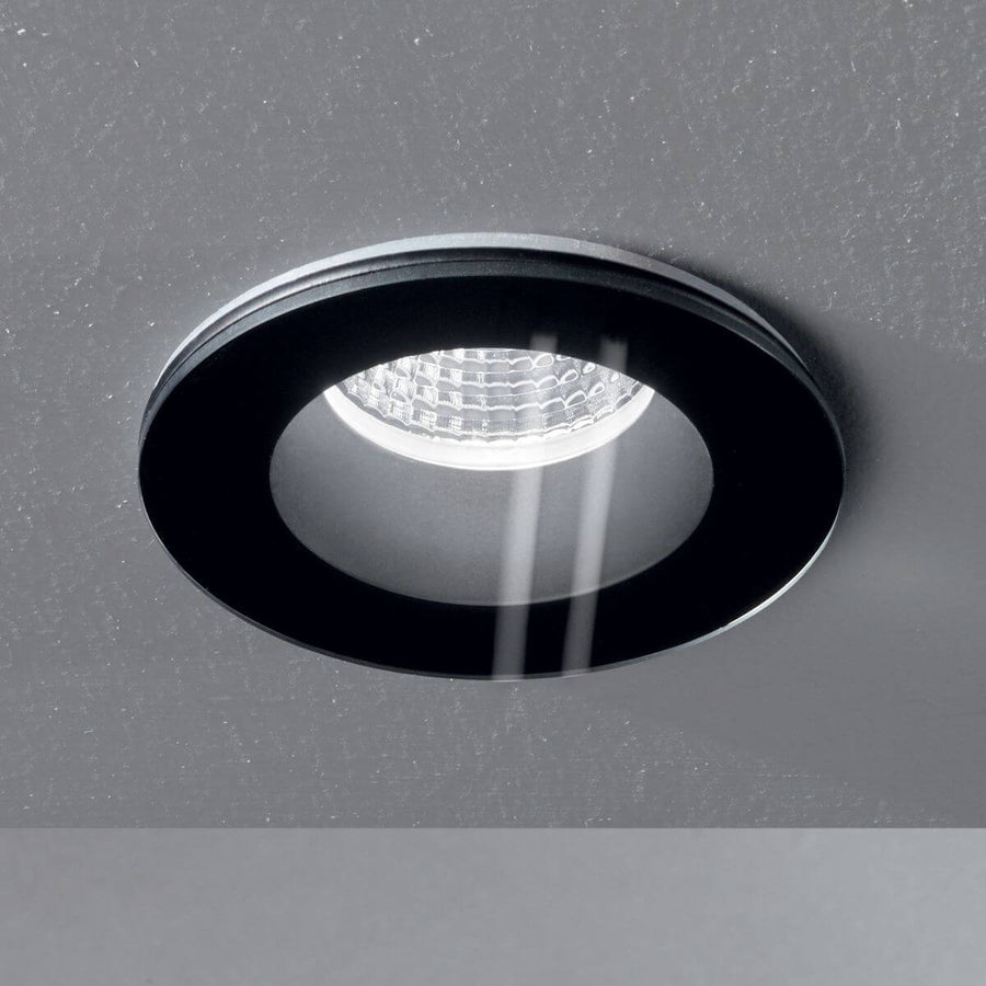 Gros plan du spot encastré dans un plafond gris, avec reflet lumineux sur la collerette noire.