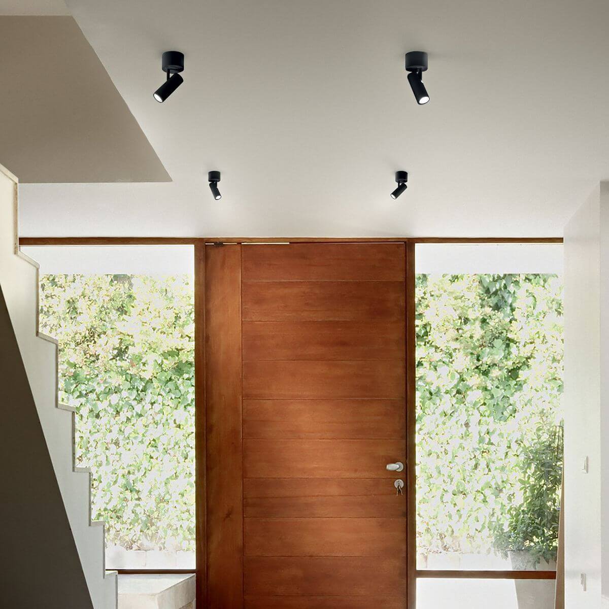 Mise en ambiance : quatre spots noirs fixés au plafond devant une porte en bois clair