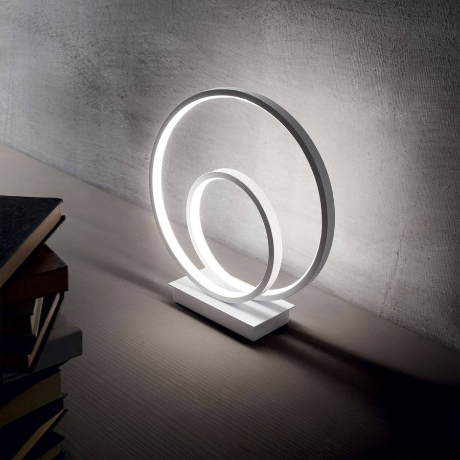 Lampe allumée posée sur un meuble, près de livres, devant un mur gris.