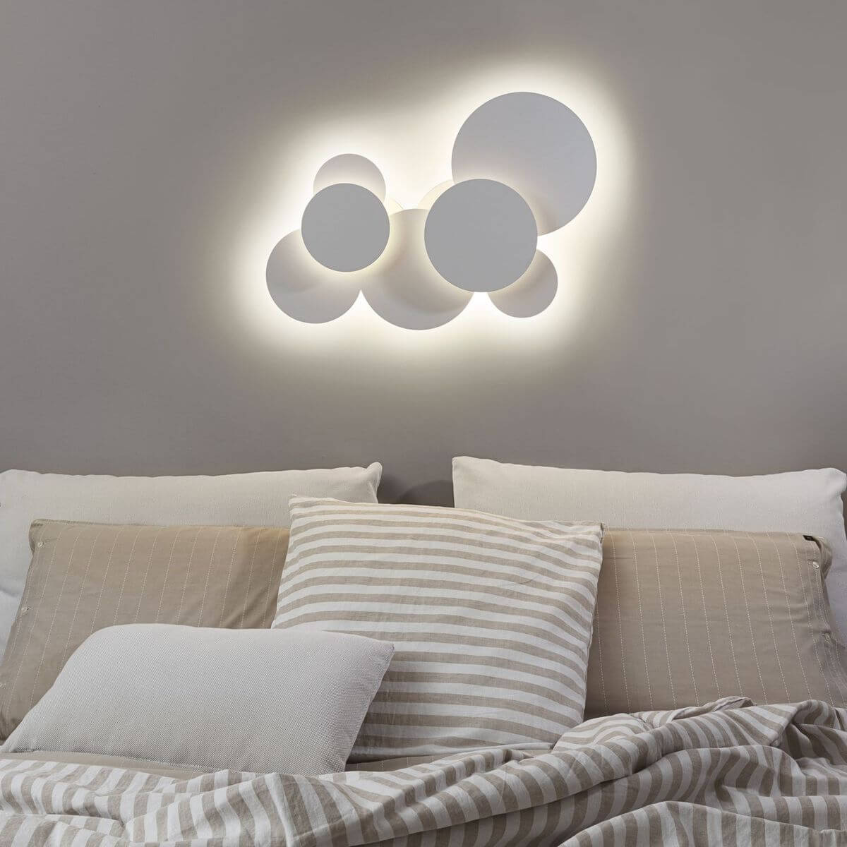 Luminaire allumé fixé au mur au-dessus d'un lit, coussins rayés beige