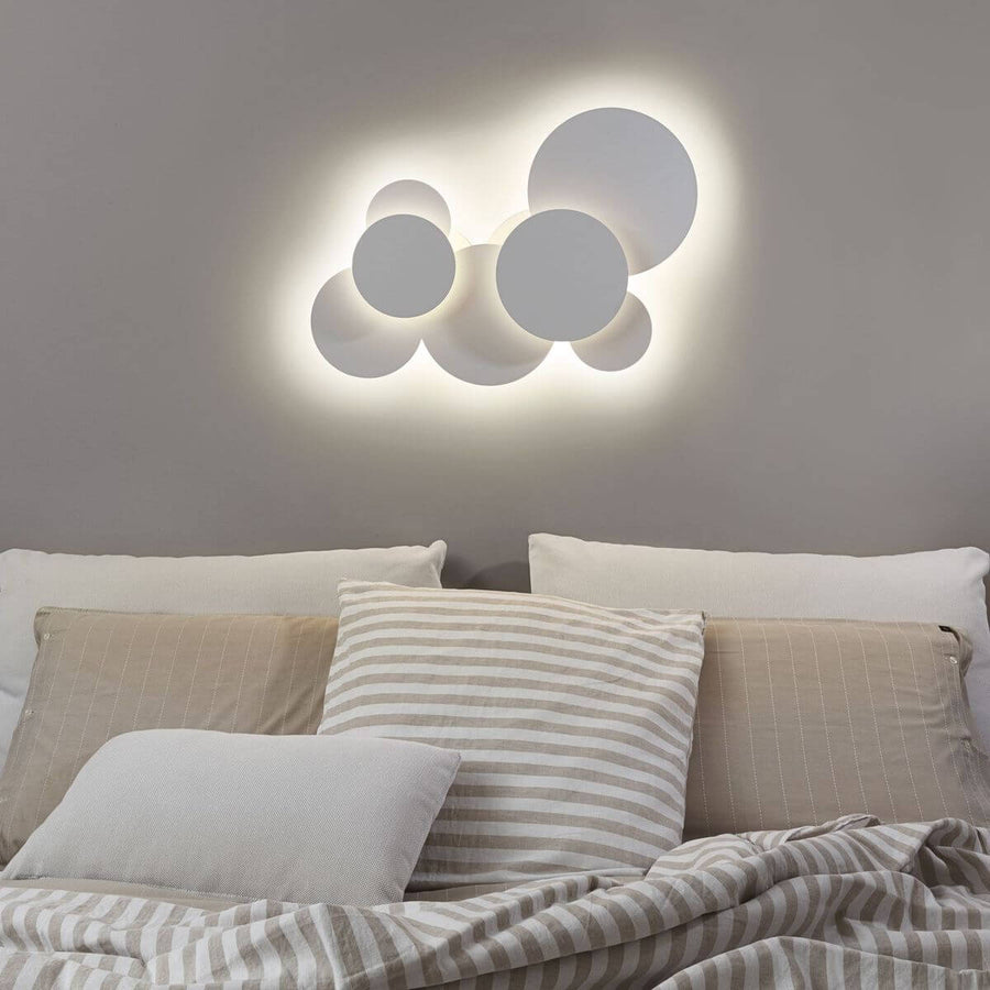 Luminaire allumé fixé au mur au-dessus d'un lit, coussins rayés beige