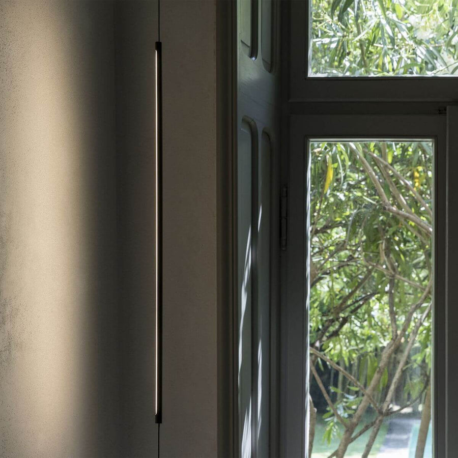 Détail du tube lumineux allumé devant une fenêtre ouverte sur des feuillages verts