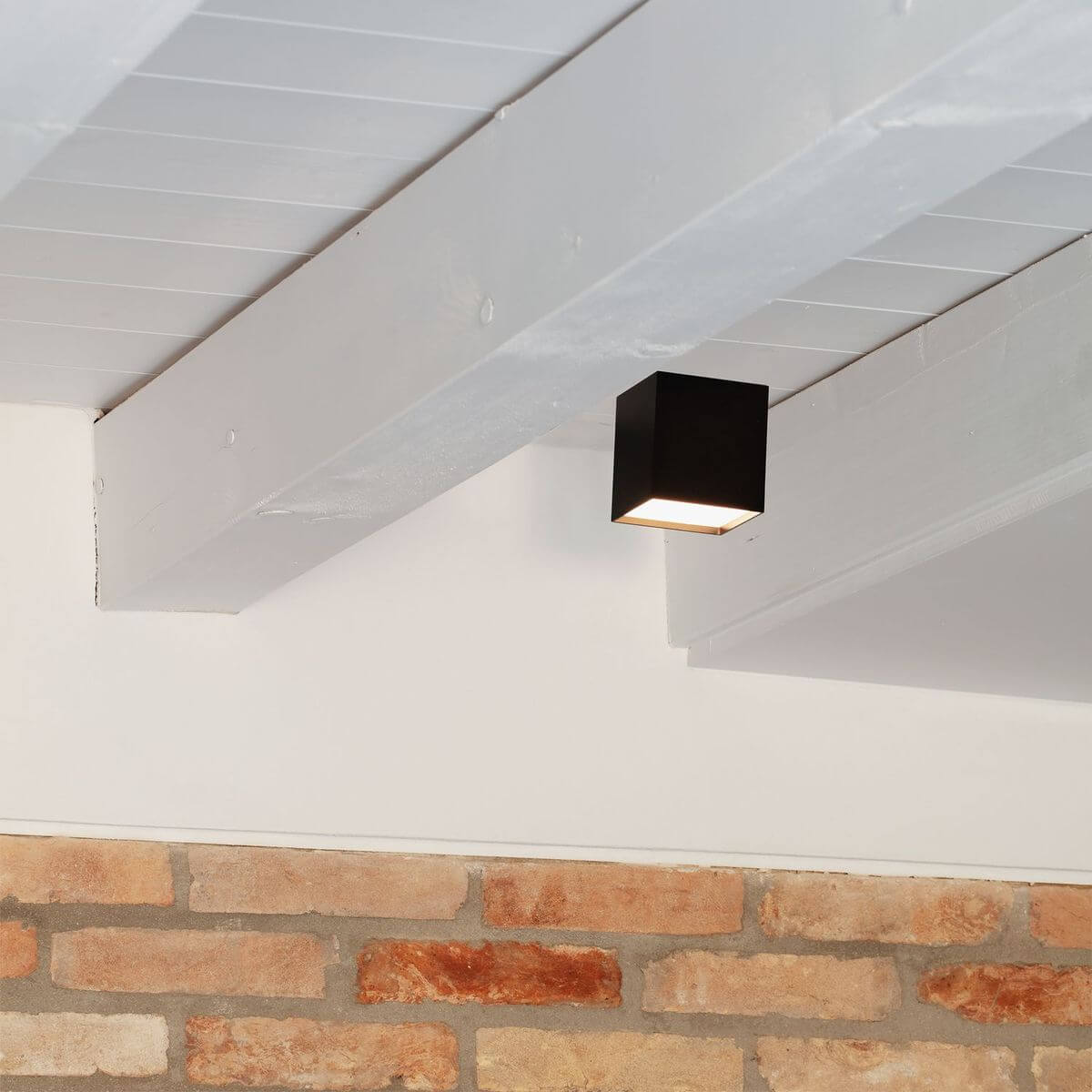 Mise en ambiance du cube noir fixé sous une poutre blanche devant mur brique