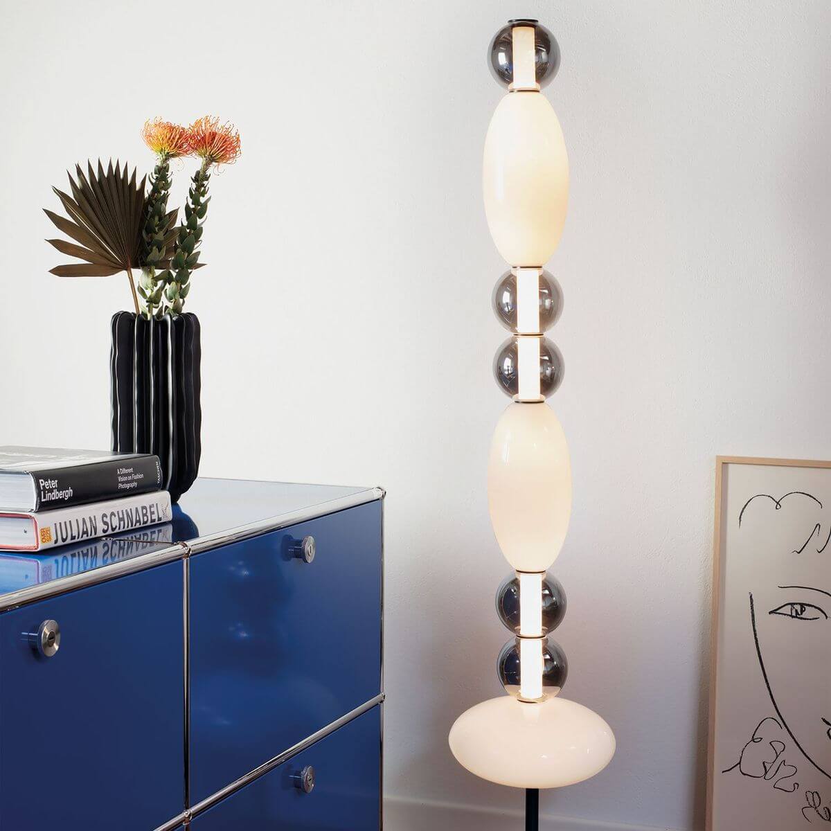 Lampadaire allumé dans un intérieur près d'une commode bleue avec vase et livres.