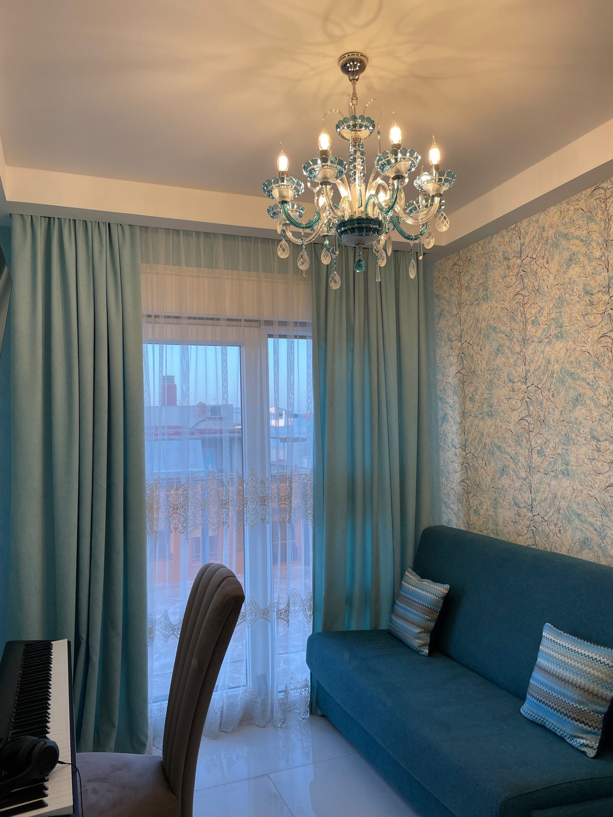 Lustre allumé suspendu devant une fenêtre, reflets sur le plafond, intérieur bleu et taupe