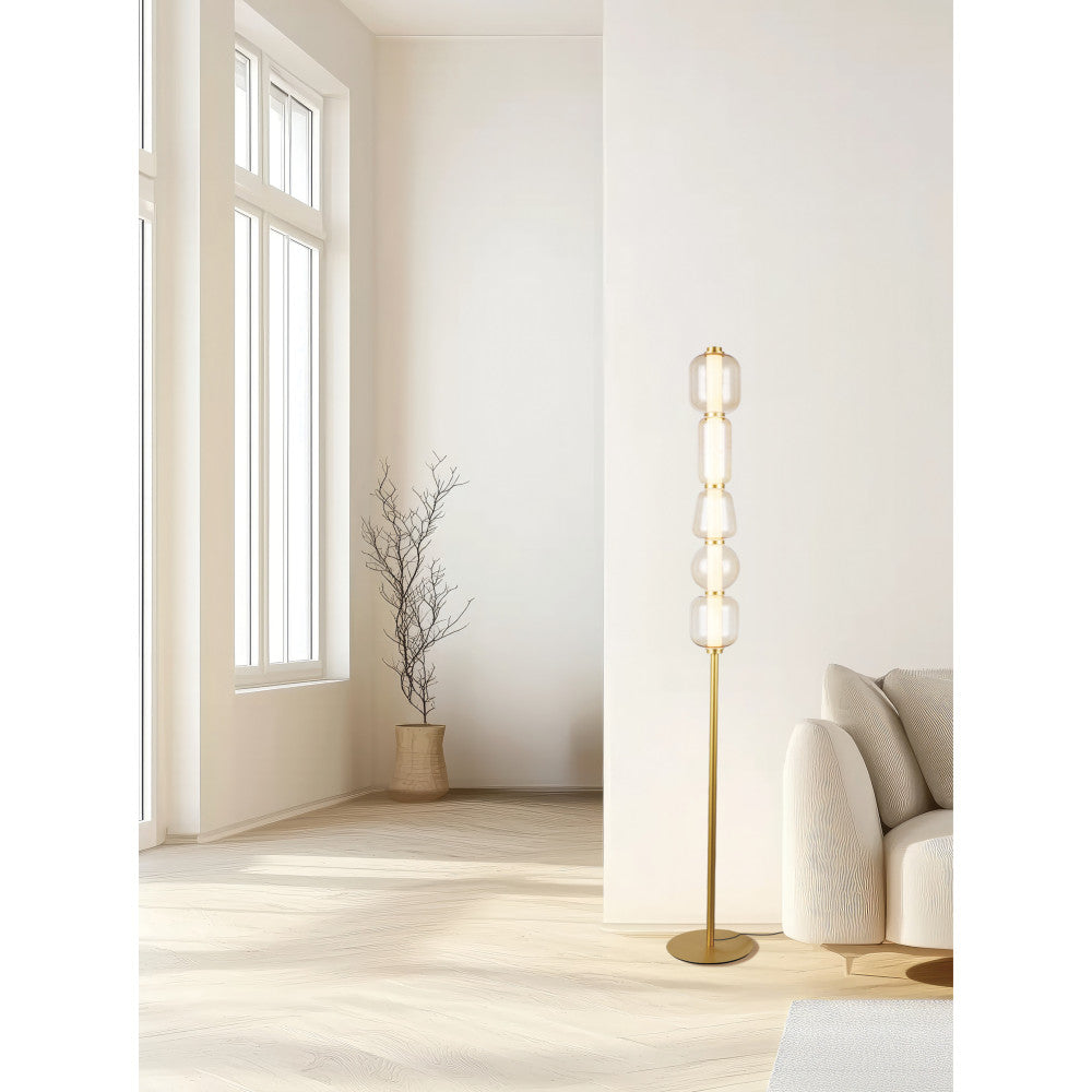 Lampadaire doré allumé dans un intérieur épuré, près d'une fenêtre et d'une plante sèche.