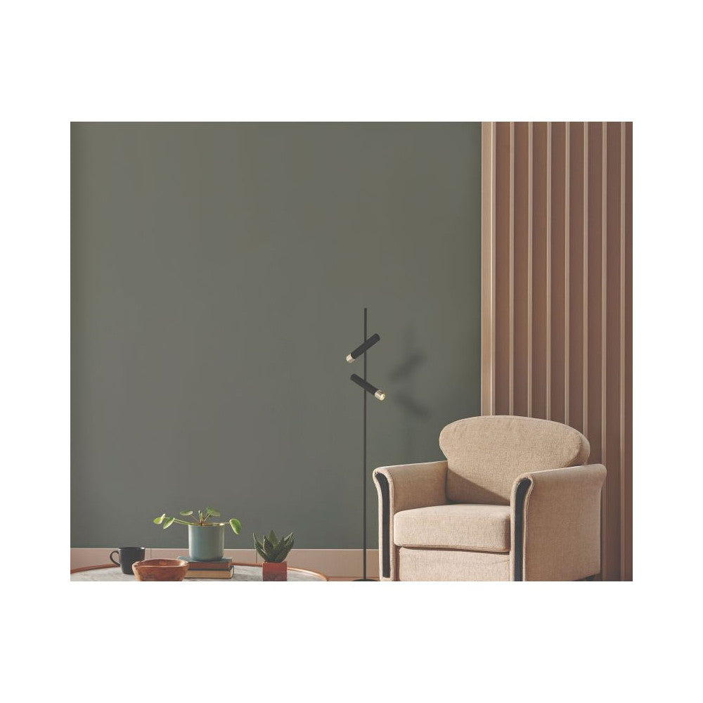 Mise en ambiance : lampadaire devant un mur vert, près d'un fauteuil beige.