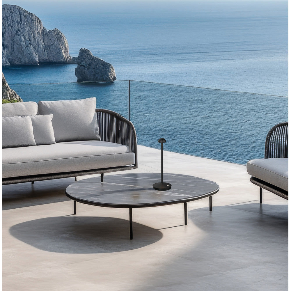 Mise en ambiance extérieure, lampe noire sur table basse devant canapé et océan