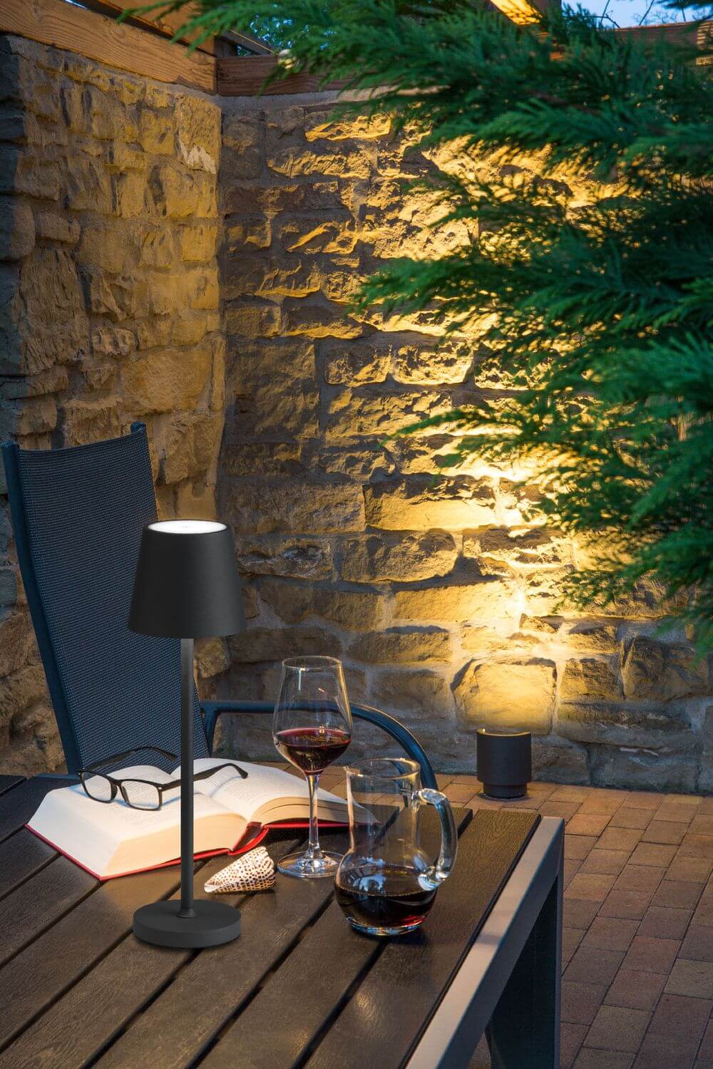 Mise en ambiance extérieure nocturne, lampe allumée sur table en bois avec verre de vin