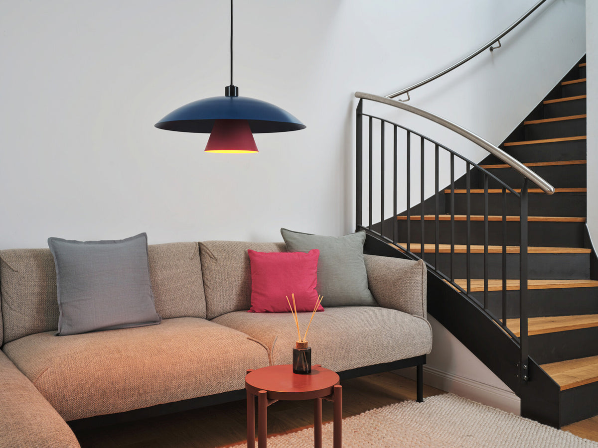 Suspension allumée au-dessus d'un canapé beige, près d'un escalier en intérieur.