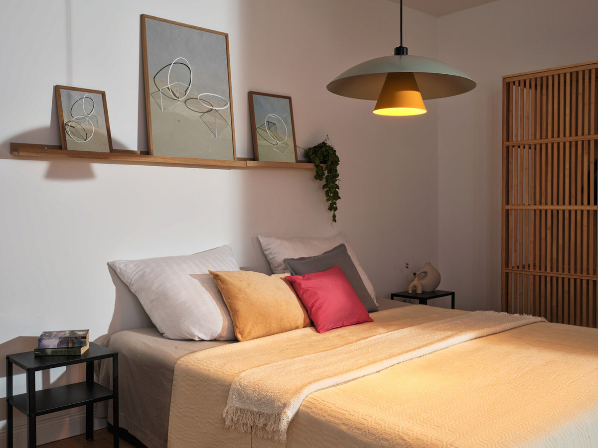 Mise en ambiance au-dessus d'un lit, suspension allumée dans une chambre claire.