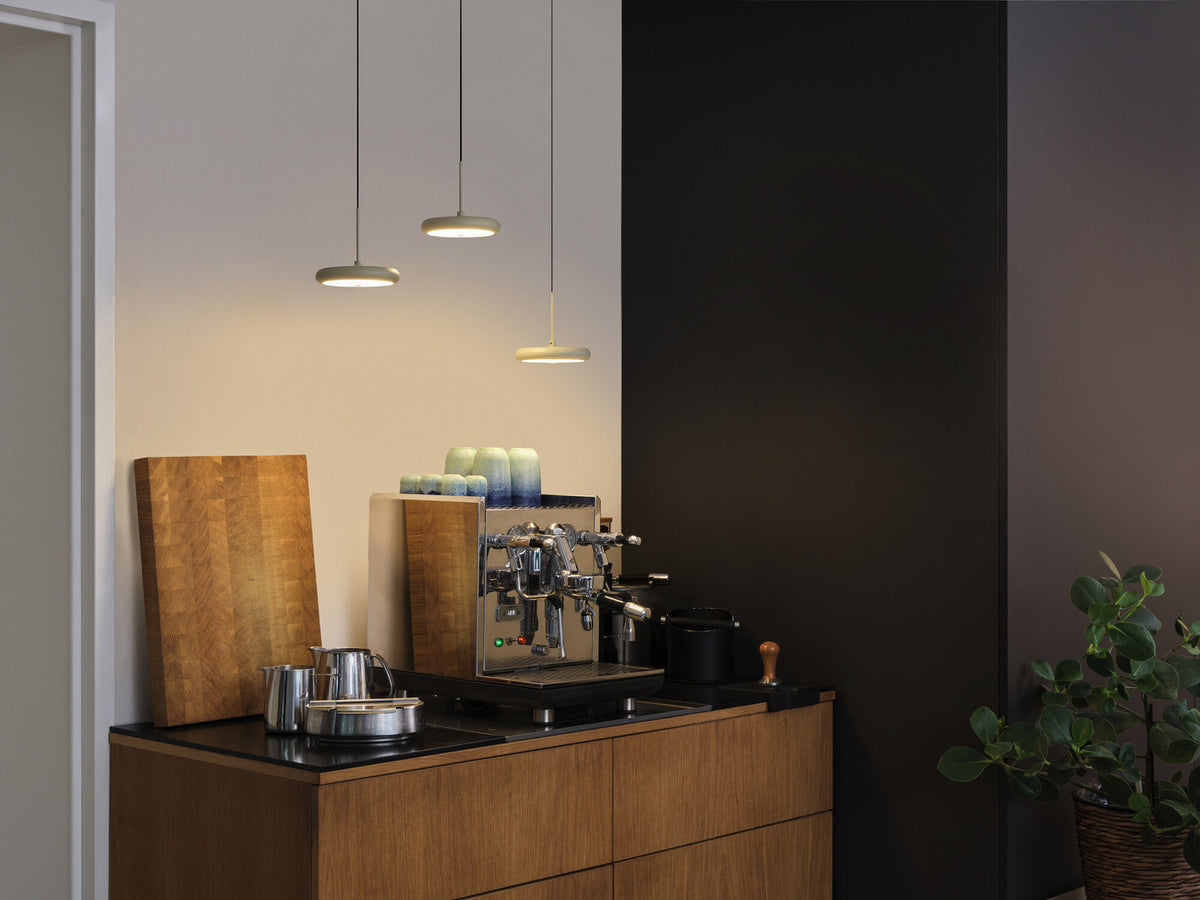 Trois suspensions beiges éclairant un coin café et un plan de travail en bois.