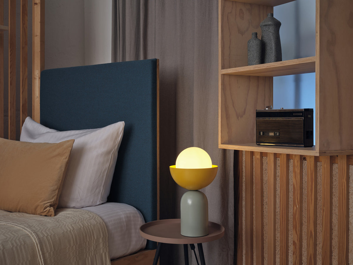 Mise en ambiance dans une chambre, lampe allumée sur une table de chevet.