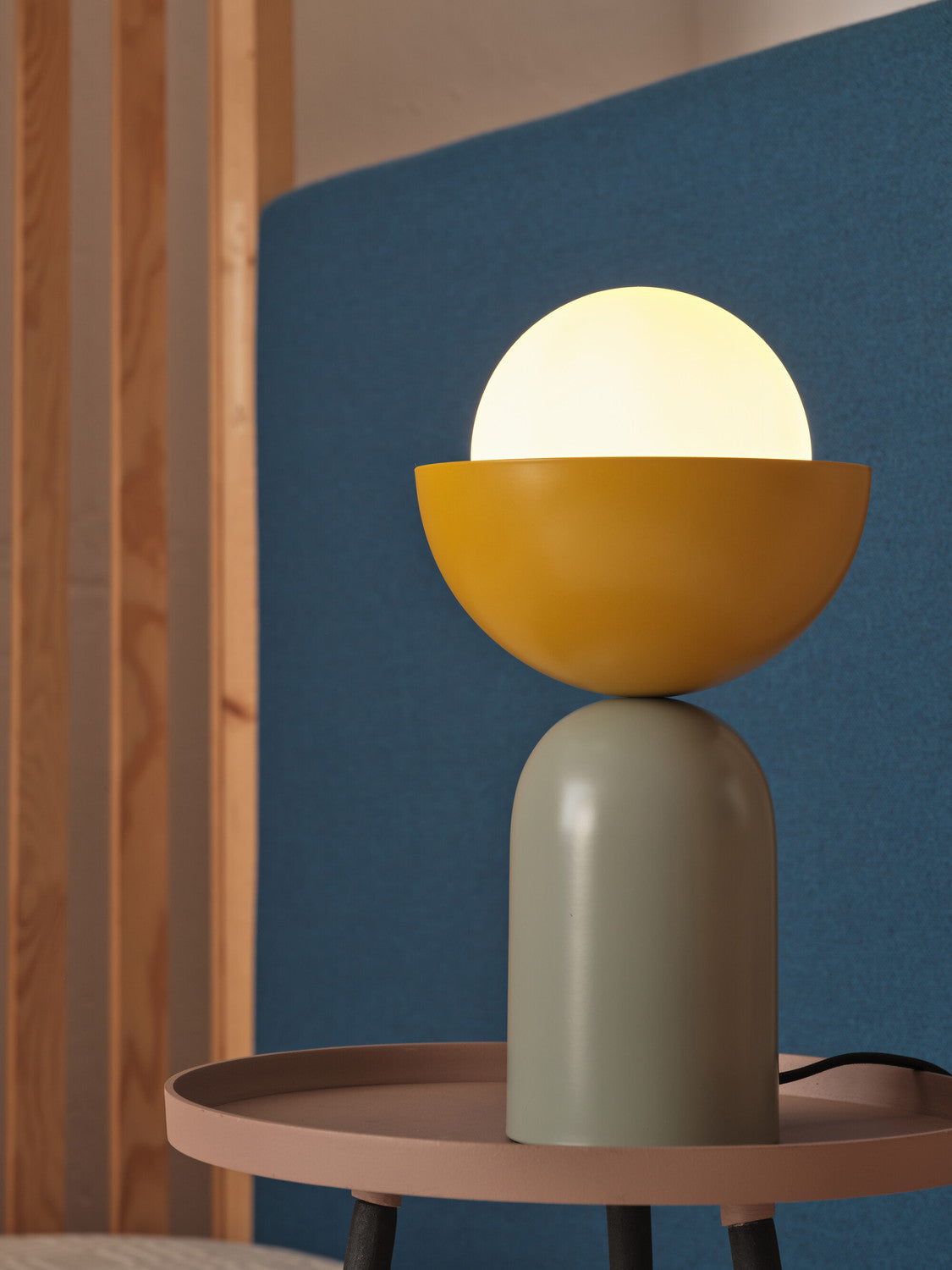 Détail de la lampe allumée, sphère lumineuse dans bol jaune sur base verte.