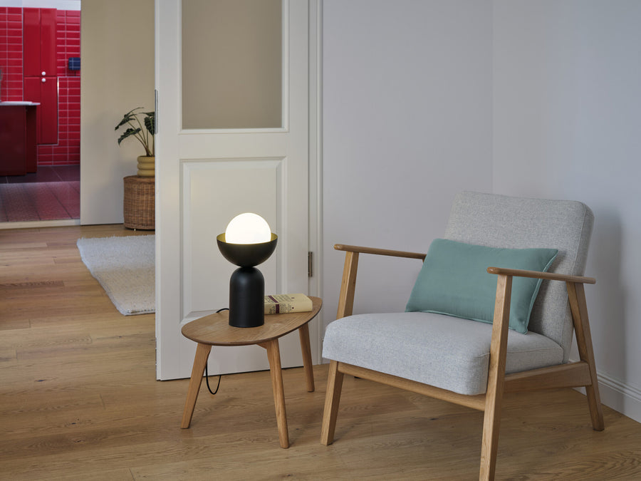 Lampe allumée posée sur une table basse près d'un fauteuil gris.