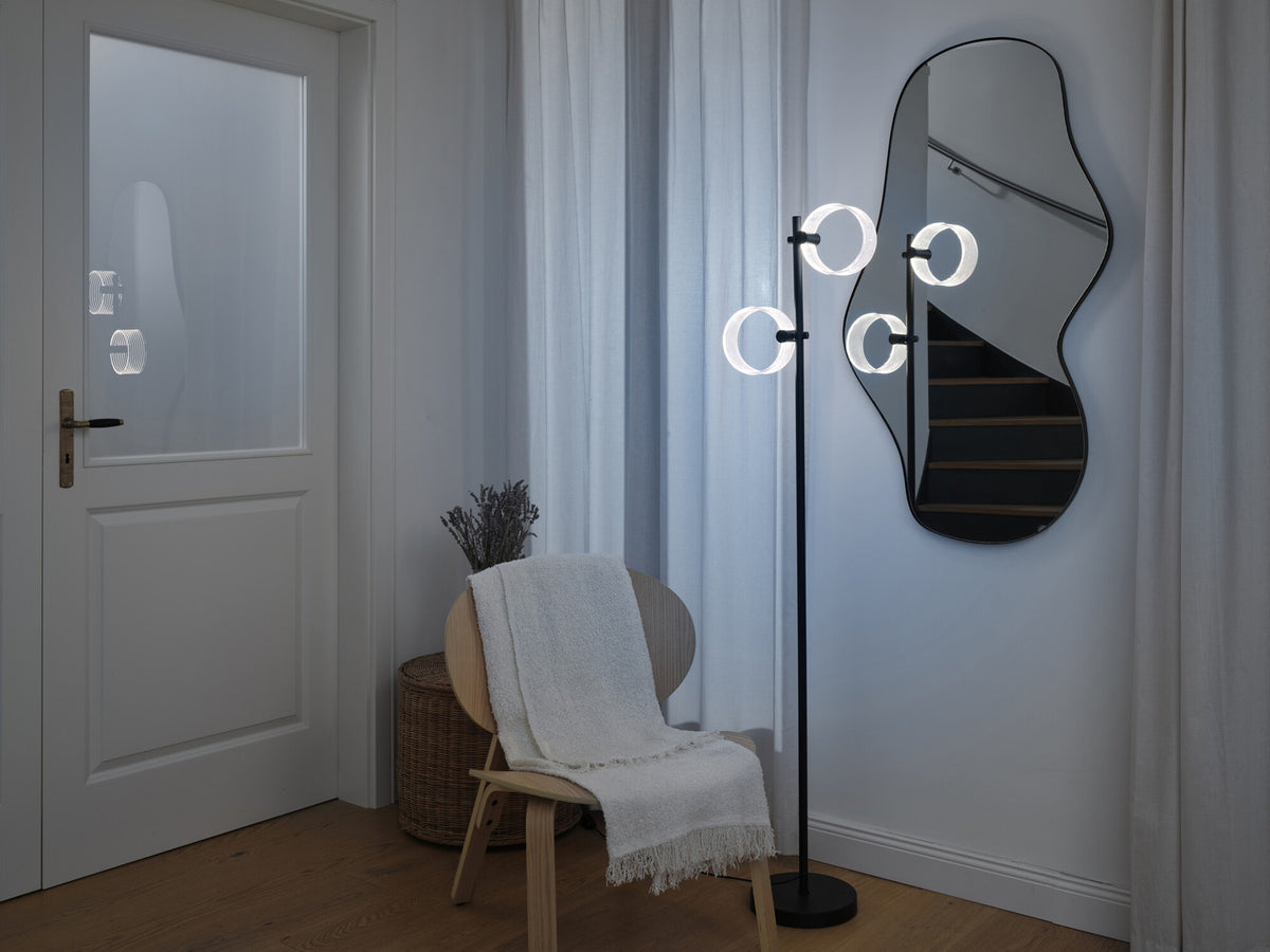 Lampadaire allumé dans une entrée devant un miroir mural et une chaise en bois