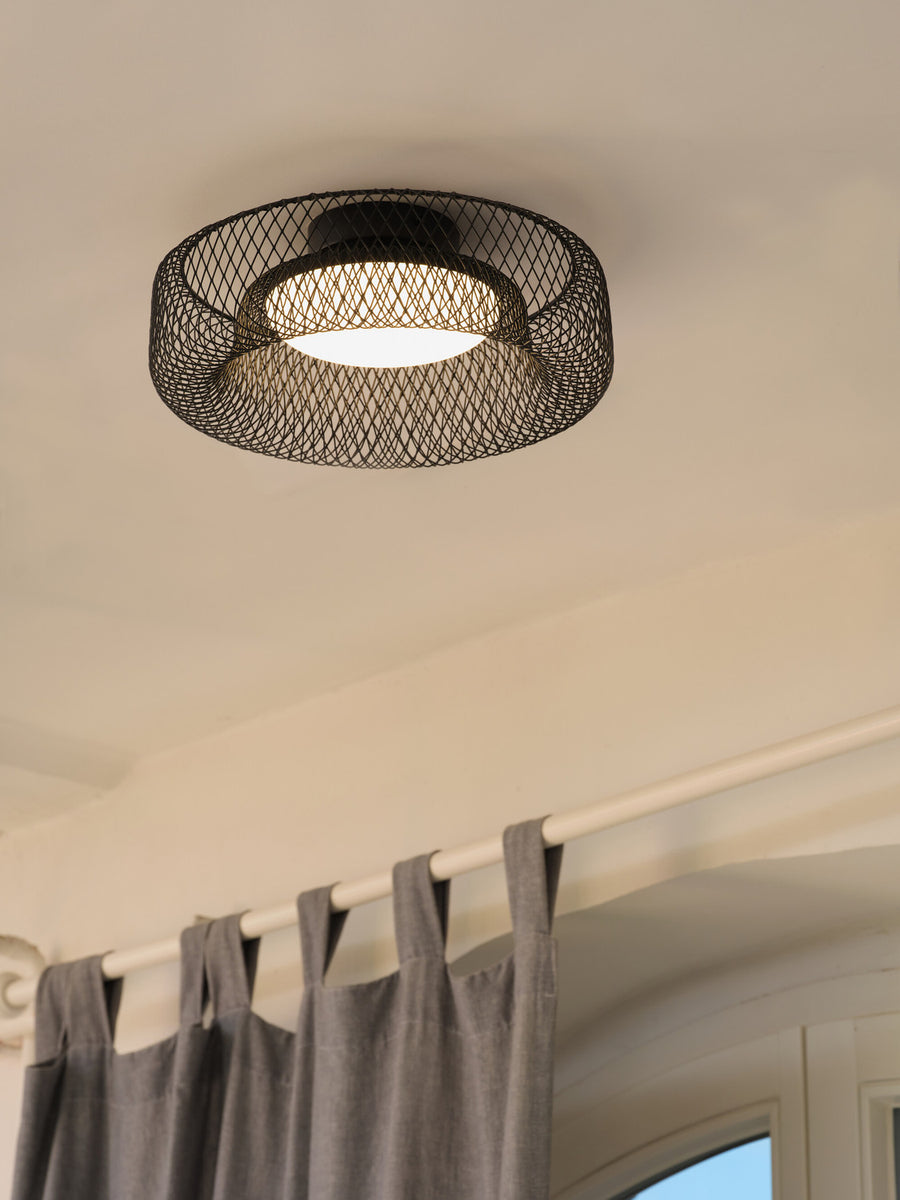 Plafonnier allumé fixé au plafond, au-dessus d'une tringle et d'un rideau gris.