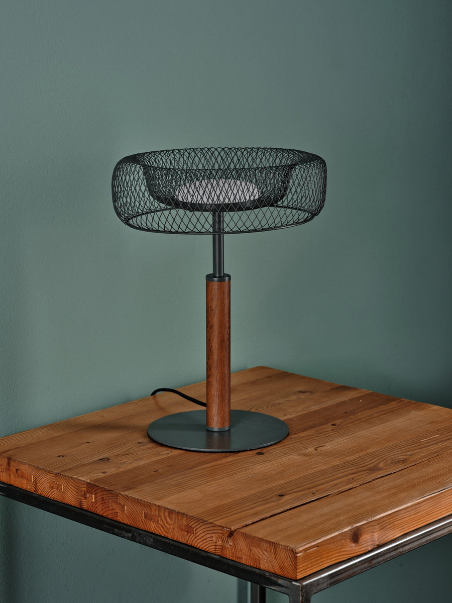 Lampe éteinte posée sur table en bois devant un mur vert, vue de trois quarts.