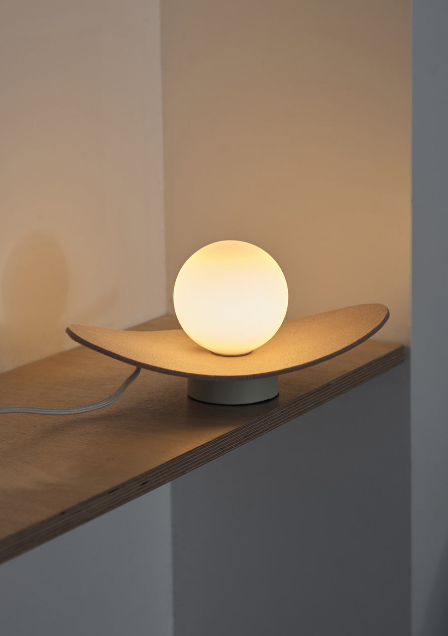 Vue rapprochée de la lampe allumée sur une étagère, câble blanc visible sur le côté.