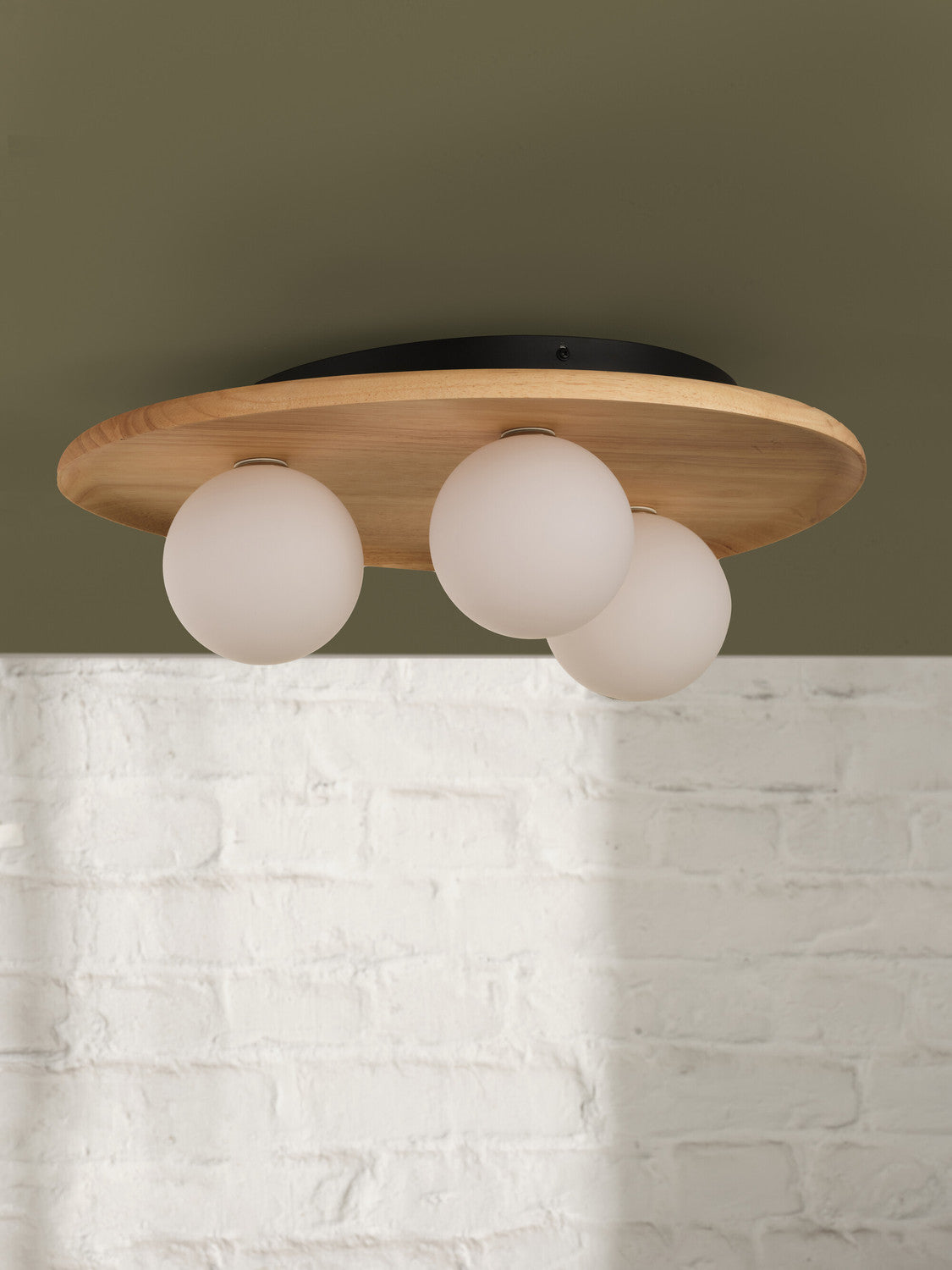 Gros plan du plafonnier en bois clair, trois globes opalins et mur de briques.