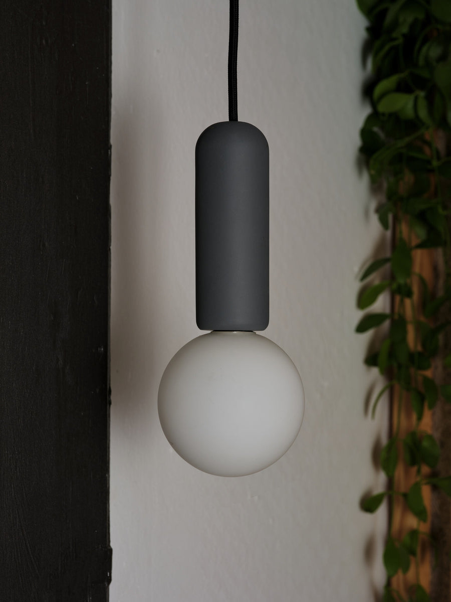 Détail rapproché du cylindre béton anthracite et du globe blanc allumé.