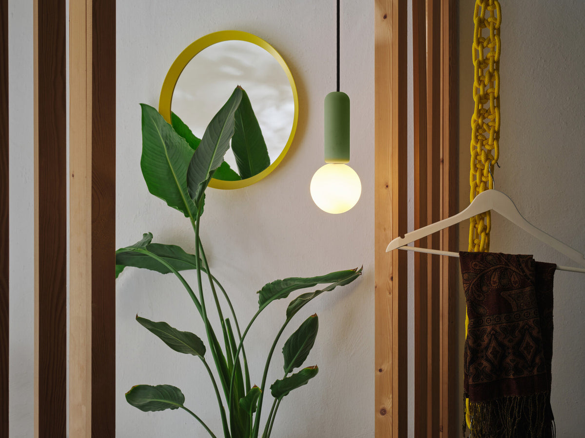 Mise en ambiance avec plante verte, miroir jaune et suspension allumée.