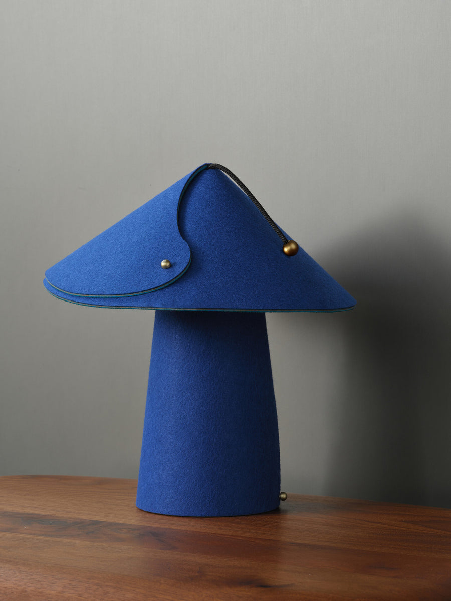Lampe bleue vue de face, abat-jour en feutre replié et fermeture à glissière apparente.