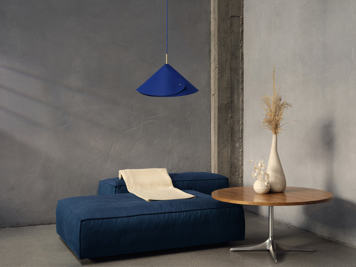 Mise en ambiance dans un salon gris, suspension bleue au-dessus d’un canapé.